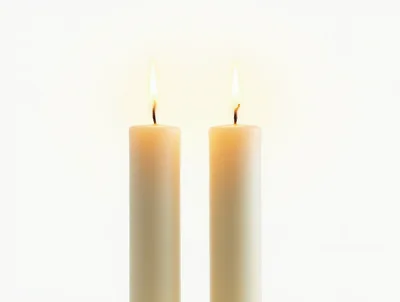 Two Lit White Candles Against A Plain Background