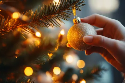 Hand Placing A Golden Ornament On A Christmas Tree