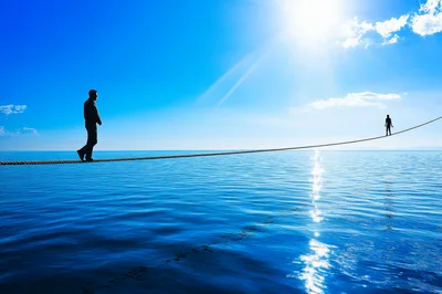 Silhouetted Figures Walking On A Tightrope Over Ocean