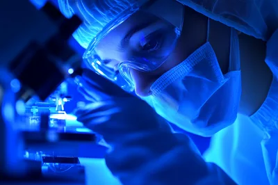 Scientist Examining Samples Under Microscope In Laboratory