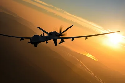MQ-9 Reaper Drone Flying Over Mountainous Landscape At Sunset
