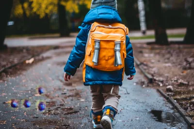 Young Child Walking Outdoors With A Yellow Backpack