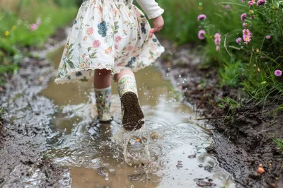Child Wearing Floral Boots Splashing In A Muddy Puddle