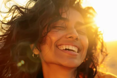 Happy Woman With Curly Hair Smiling In Golden Sunlight