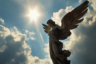 Stone Angel Statue Against Sunlit Cloudy Sky