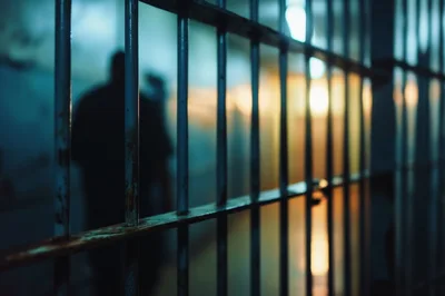Silhouette Of A Prisoner Behind Metal Jail Bars