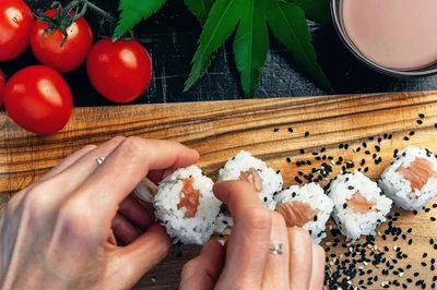 Hands Arranging Fresh Salmon Sushi Rolls On Wooden Board