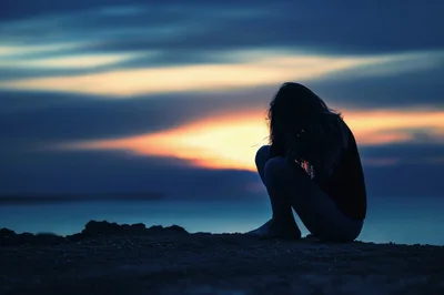 Silhouette Of A Sad Woman Sitting Alone At Sunset