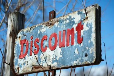 Weathered Discount Sign Outdoors Against Blue Sky