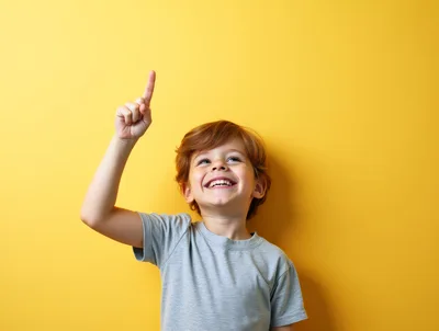 Happy Young Boy Pointing Upwards Against Yellow Background
