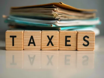 Wooden Blocks Spelling Taxes With Stacked Paperwork