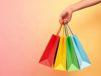 Hand Holding Colorful Shopping Bags Against Gradient Background