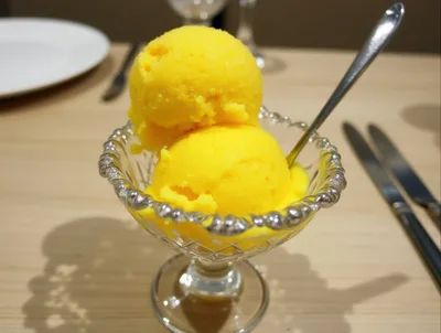 Two Scoops Of Bright Yellow Mango Sorbet In Crystal Bowl