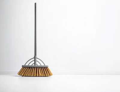 A Single Broom Standing Against A White Wall