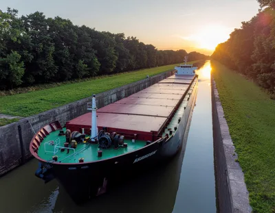 Cargo Ship Navigating Through A Narrow Canal At Sunset