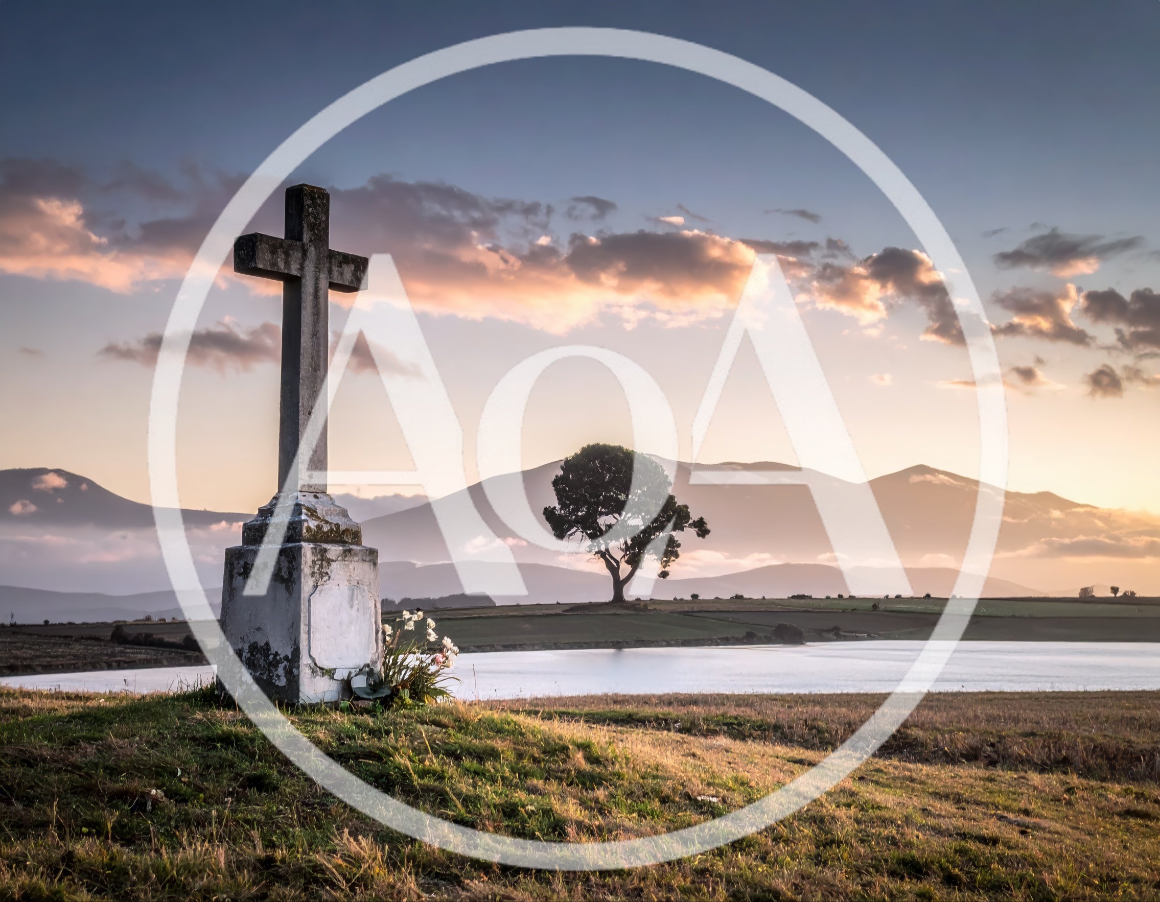 Stone Cross Monument Overlooking A Serene Lake At Sunset
