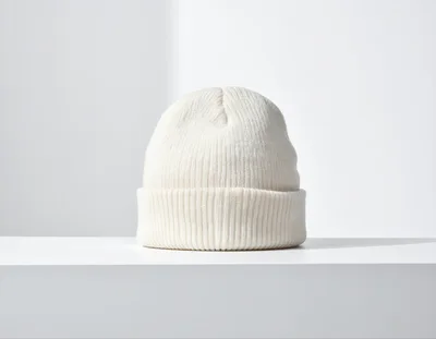 White Knitted Beanie Hat On A White Surface