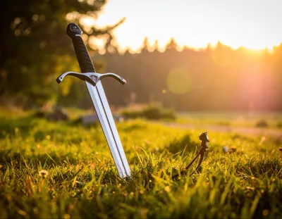 Medieval Sword Stuck In The Grass At Sunset