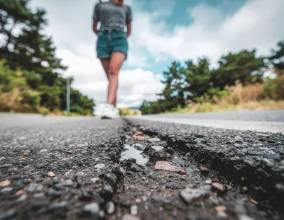 Woman Walking Along A Damaged Asphalt Road
