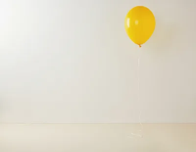 Single Yellow Balloon Floating Against A Plain Wall