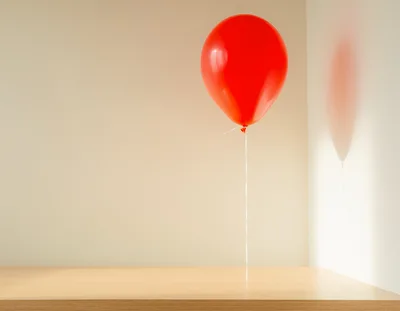 Single Red Balloon Floating Above Wooden Table
