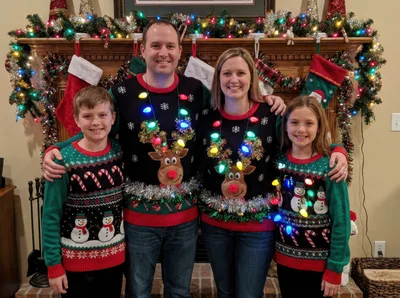 Family Posing In Matching Christmas Sweaters By Fireplace