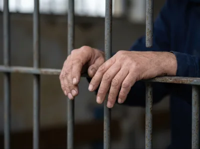 Close Up Of Prisoner Hands Gripping Metal Jail Bars