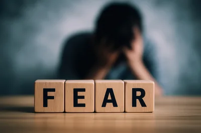 Wooden Blocks Spelling Fear With Distressed Person In Background