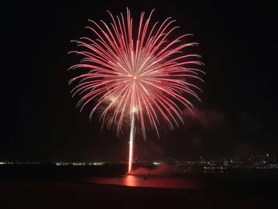 Large Red Fireworks Bursting Over Dark Water