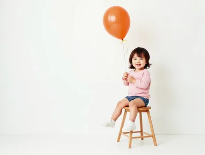 Toddler Girl Sitting on Stool Holding Orange Balloon