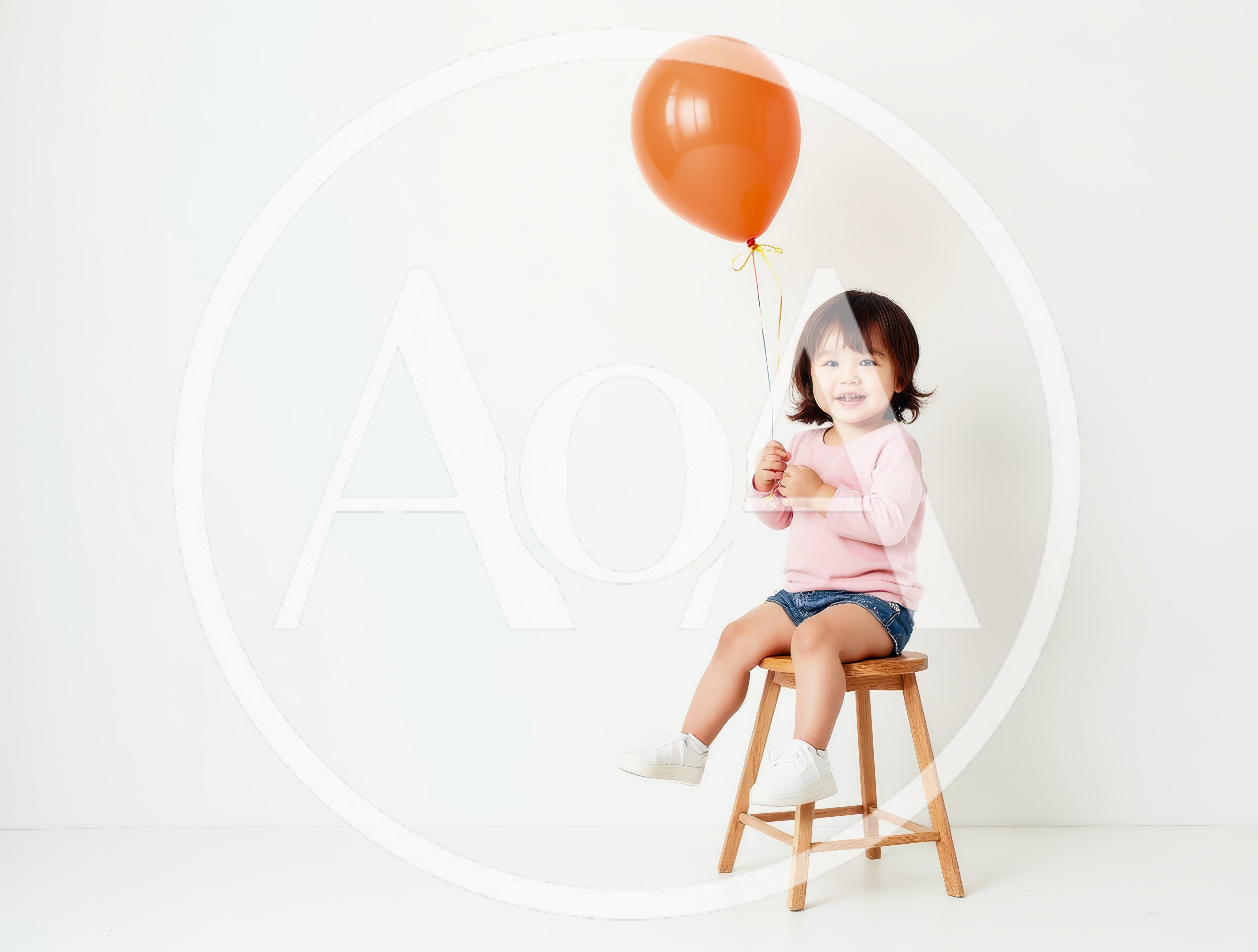 Toddler Girl Sitting on Stool Holding Orange Balloon