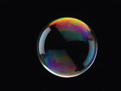 Single Iridescent Soap Bubble Floating Against Black Background