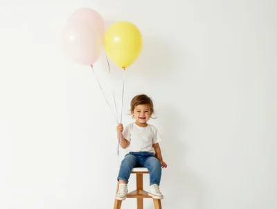 Happy Toddler Sitting on Stool Holding Balloons