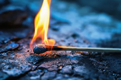 Burning Matchstick Resting On A Dark Textured Surface