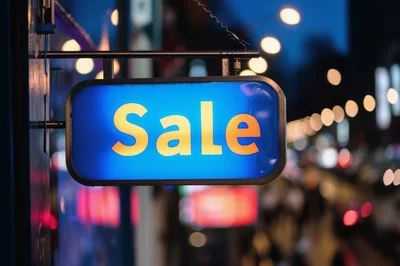 Illuminated Blue Sale Sign Hanging On City Street
