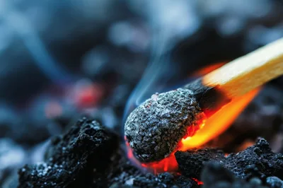 Burning Matchstick Resting On Glowing Charcoal Embers