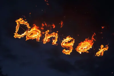 Flaming Danger Sign Written In Fire Against Dark Sky