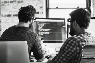 Two Software Developers Collaborating On Code In Office