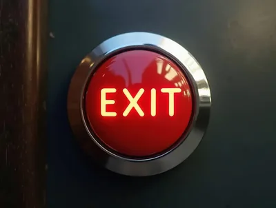 Illuminated Red Exit Push Button On Dark Wall