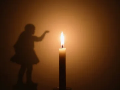 Shadow Of A Child Reaching Toward A Candle Flame