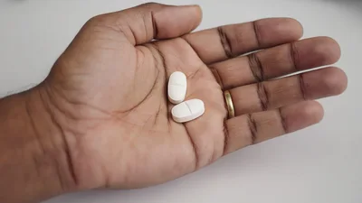 Person Holding Two White Oval Pills In Palm