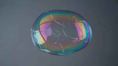 Iridescent Soap Bubble Bursting Against A Grey Background