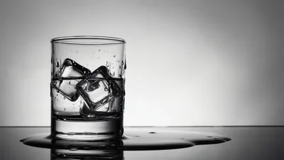 Glass Of Whiskey With Ice Cubes On Reflective Surface