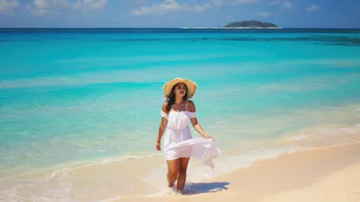 Young Woman Walking Along Tropical Beach In White Dress