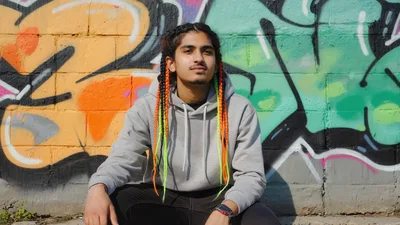Young Man With Colorful Braids Sitting Against Graffiti Wall