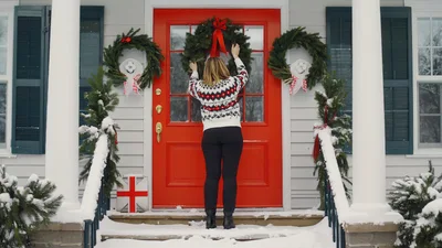 Woman Hanging Christmas Wreath On Red Front Door