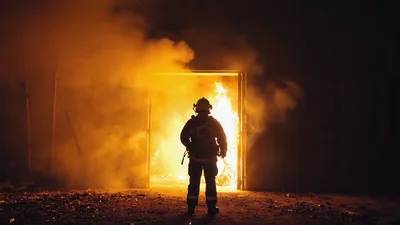 Firefighter Standing Before A Burning Doorway