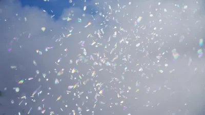 Iridescent Confetti Floating Against A Cloudy Blue Sky