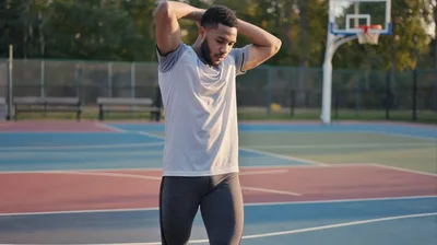 Athletic Man Stretching Arms On Outdoor Basketball Court