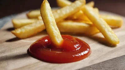 French Fry Dipped In Ketchup On Wooden Board